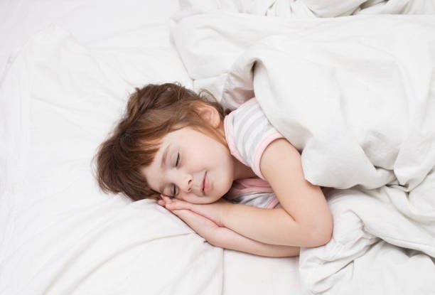 A girl of 4 years is sleeping calmly on the bed. 